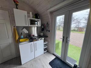 a kitchen with white cabinets and a door to a yard at Kelp Drift, Coastal Pod, near Oldshoremore Beach in Rhiconich