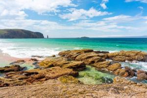a beach with rocks and the ocean on a sunny day at Kelp Drift, Coastal Pod, near Oldshoremore Beach in Rhiconich