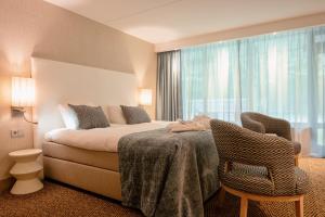 a bedroom with a bed and a chair and a window at Van der Valk Hotel Hollands Kroon in Wieringerwerf
