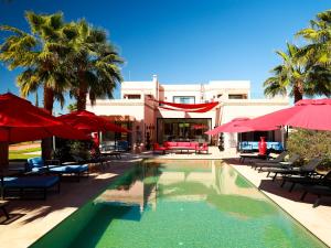 a swimming pool with red umbrellas and tables and chairs at Villa des iris Domaines NAJMA in Marrakesh