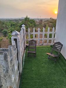 two chairs and a fence with the sunset in the background at ViRa Farm in Sūlagiri