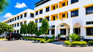 a large white building with trees in a parking lot at Tum Hotel & Conferencing in Mombasa