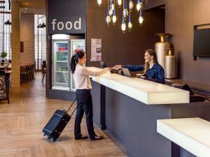 a woman with a suitcase standing at a food counter at Mercure Sao Bernardo Do Campo in São Bernardo do Campo