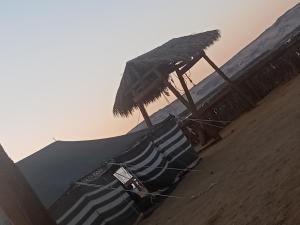 a beach with a straw umbrella and chairs on the sand at safari book in Bawati