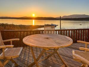 a wooden table and chairs on a deck with a sunset at Creag Bheag in Appin