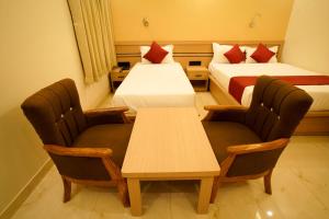 two beds in a room with two chairs and a table at Shree Goljyu Palace in Almora