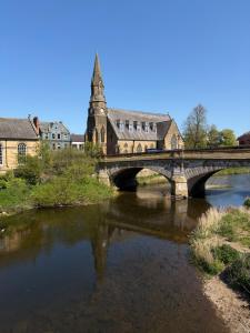 a bridge over a river with a building and a church at Riverside Stay in Morpeth