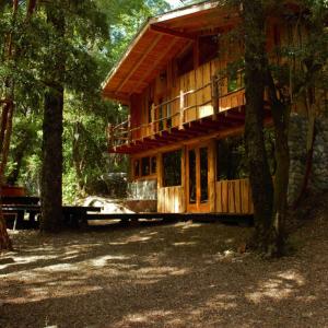 a large wooden cabin in the middle of trees at Entre arrayanes lodge in Curarrehue