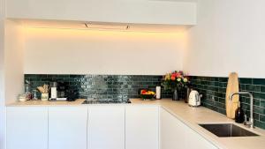 a kitchen with white cabinets and green tiles at House C - North Sea Stays in De Haan