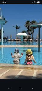 two people sitting in the water at a swimming pool at The Noverian Scenic Crete 5 Star Hilltop Villa Resort & Spa in Malia