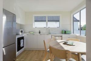 a white kitchen with a table and a table and chairs at The Sun Deck Five Star Focused Downtown Location in Mount Maunganui