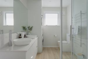 a white bathroom with two sinks and a shower at The Sun Deck Five Star Focused Downtown Location in Mount Maunganui