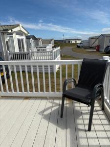 a black chair sitting on a porch with a white fence at Dune View Caravan in Lossiemouth +17 photos