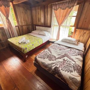 two beds in a room with wooden walls at Hostal Vista Verde in Mindo