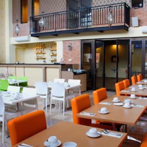 un restaurante con mesas de madera y sillas naranjas en D'Kalpa Hotel Demangan Yogyakarta, en Yogyakarta