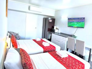 two beds in a room with a tv on the wall at Tropical Gateway Motor Inn in Rockhampton