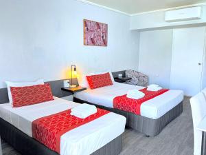 two beds in a hotel room with red pillows at Tropical Gateway Motor Inn in Rockhampton