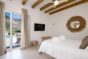 a white bedroom with a bed and a balcony at Lithos Suites Sifnos in Kamares