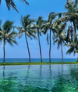 a pool with palm trees in front of the ocean at Louka Beach Bali in Tianyar