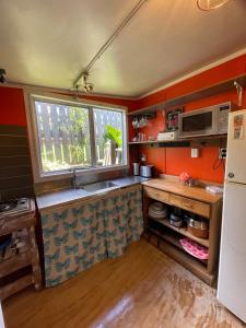 a small kitchen with orange walls and a window at Le Bach - Rustic Central Raglan in Raglan
