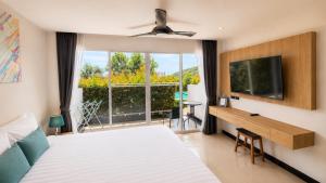 a bedroom with a bed and a tv and a window at Santosa Hotel & Welness Center in Kata Beach