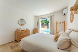 a white bedroom with a bed and a window at Le Cabanon de Val in Gassin