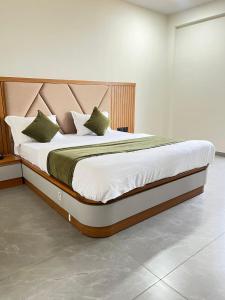 a bedroom with a large bed with white sheets and green pillows at Hotel Sun Park Vadodara in Vadodara