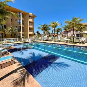 a swimming pool at a resort with chairs and palm trees at Loft no Refúgio do Sahy in Mangaratiba