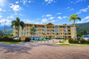 a large yellow building with palm trees in a parking lot at Loft no Refúgio do Sahy in Mangaratiba
