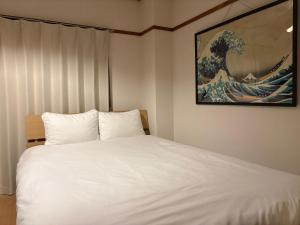 a bedroom with a white bed with a painting on the wall at 指宿 潮音 Ibusuki Shione in Ibusuki