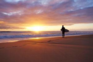 a man walking on the beach with a surfboard at Surf & Sauna Bud House in Longeville-sur-Mer