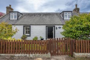 a white house with a wooden fence at Shop Cottage, Findhorn in Findhorn