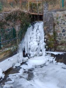 a waterfall covered in snow next to a stone wall at Moulin de la Varenne in Saint-Saturnin +7 photos