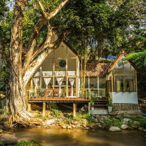 a house with a deck next to a river at The ForRest Peace Forest แม่กำปอง in Ban Huai Kaeo
