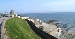 a group of people walking along a wall next to the ocean at Coastal Apartment in Malahide +13 photos