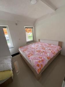a bedroom with a bed with a pink comforter and two windows at Vila Tigani in Peje