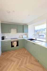 a kitchen with green cabinets and a sink at Coastal Cottage NC500 in Castletown