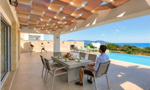 a man sitting at a table on the patio of a house at Marea Villas Heated Pool in Dhrámia