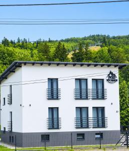 a white building with black balconies and trees at Apartamenty Pod Wyciągiem in Wisła