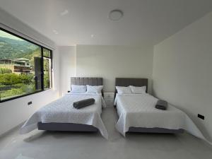 two beds in a white room with a large window at DLiam Home in Baños