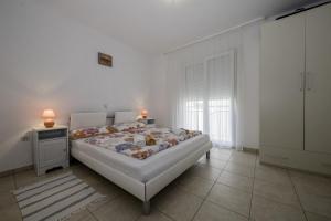 a white bedroom with a bed and a window at Apartmani Leovac in Lopar