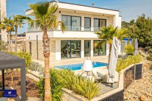 a house with a palm tree and a swimming pool at Primosten Hills West - Branded Luxury Villa in Primošten