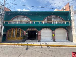 a green building with white garage doors on a street at Hotel Los Arcos in Pénjamo