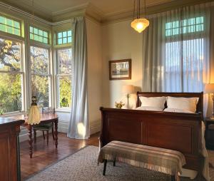a bedroom with a bed and a desk and windows at The Vicarage Boutique Bed and Breakfast Oamaru in Oamaru