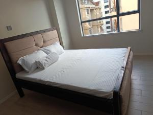 a bed with white sheets and pillows in a room with a window at Leo residences 1 in Eldoret