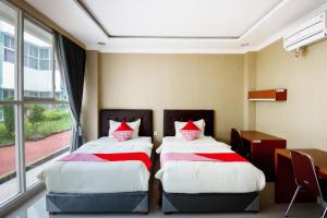 two beds in a room with a desk and a window at Collection O 3431 Hotel Alpha Bandara in Palembang +24 photos