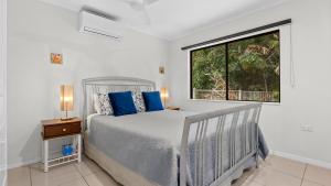 a bedroom with a bed with blue pillows and a window at Honeybee House Cottage in the Rainforest in Kuranda