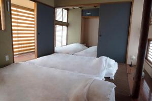 two beds with white sheets in a room with windows at goemon-inn in Akita