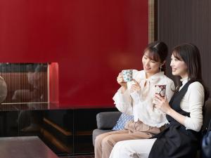 two women sitting next to each other holding coffee cups at Hotel Resol Trinity Kanazawa in Kanazawa