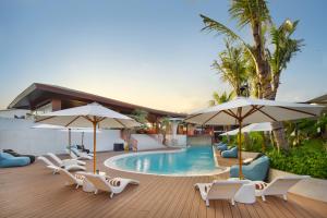 a swimming pool with chairs and umbrellas and a pool at Maha Resort Bali in Canggu
